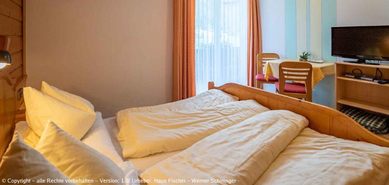 Eines unserer Zimmer mit Blick vom Bett auf den Balkon, einen Tisch mit zwei Sesseln und den Fernseher.