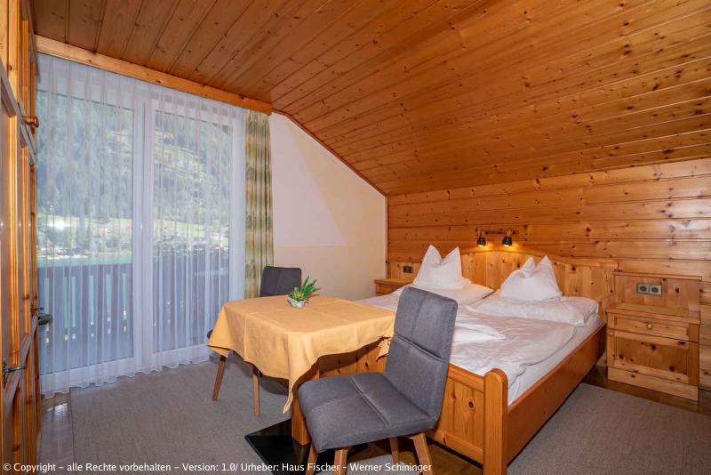 Eines unserer Zimmer mit Blick auf den Balkon und einen Tisch mit zwei Sesseln vor dem Bett.