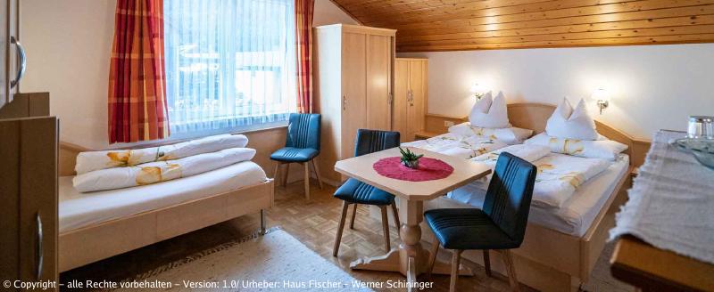 Eines unserer Zimmer mit Blick auf ein Einzelbett, einen Tisch mit zwei Sesseln, dahinter ein Bett mit einem Kasten und einem weiteren Sessel.