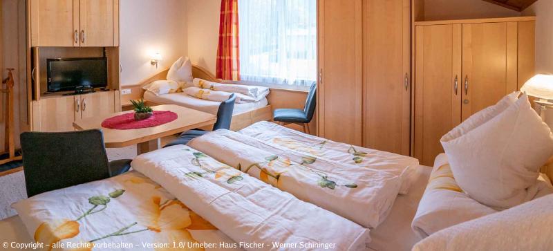 Eines unserer Zimmer mit Blick auf ein Einzelbett, einen Tisch mit zwei Sesseln, dahinter ein Bett mit einem Kasten und einem weiteren Sessel. (aus einem anderen Winkel)