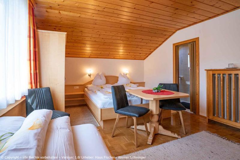 Eines unserer Zimmer mit Blick auf ein Einzelbett, einen Tisch mit zwei Sesseln, dahinter ein Bett mit einem Kasten und einem weiteren Sessel. (aus einem anderen Winkel)