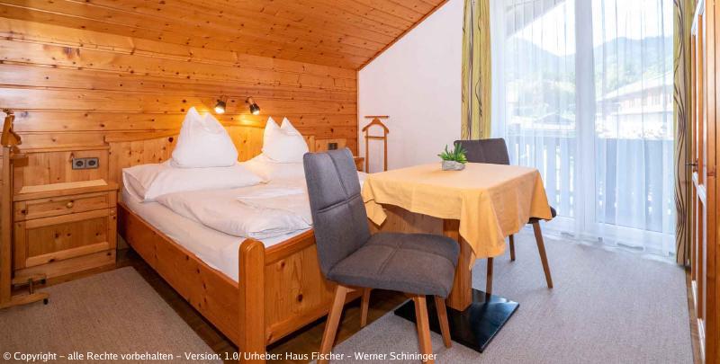 Eines unserer Zimmer mit Blick auf den Balkon und einen Tisch mit zwei Sesseln vor dem Bett. (aus einem anderen Winkel)