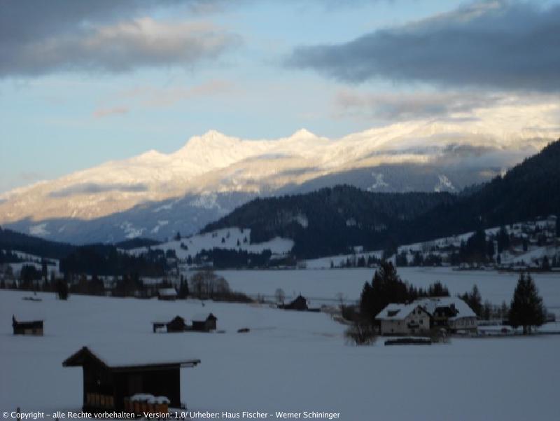 Blick auf den Weissensee mit Häusern und den Bergen im Hintergrund im Winter beim Einbruch des Abends.